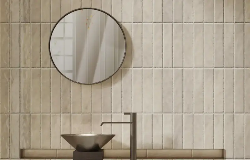 Un lavabo moderne et un miroir rond se reflètent sur un mur de toilette carrelage aux tons sable.