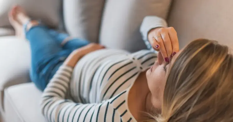 Kobieta w ciąży leży na kanapie, dotykając czoła. Zmartwienie o brak bicia serca w 8 tygodniu ciąży maluje się na jej twarzy.