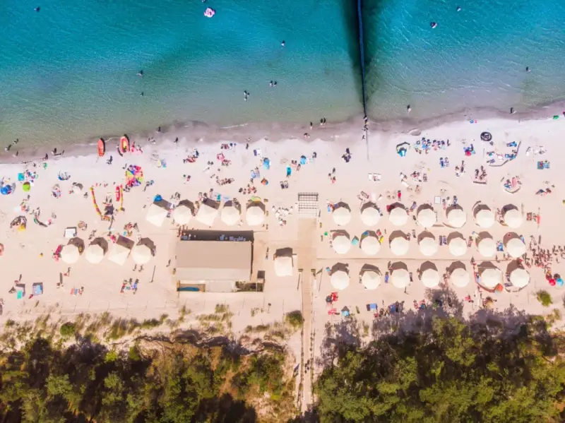 Plaża z parasolami i ludźmi, idealna na wakacje all inclusive Polska.