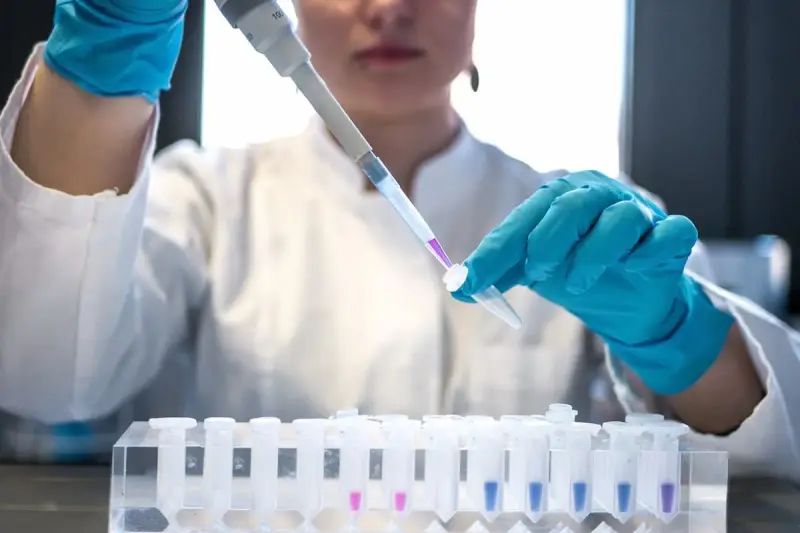 Naukowczyni w niebieskich rękawiczkach precyzyjnie pipetuje fioletowy płyn do probówki. To kluczowy etap w badaniach nad leczeniem biologicznym.