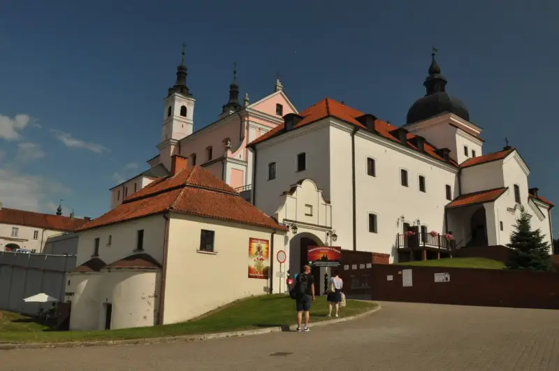 Białe budynki z czerwonymi dachami, wieże i kopuła tworzą malowniczy klasztor kamedułów.