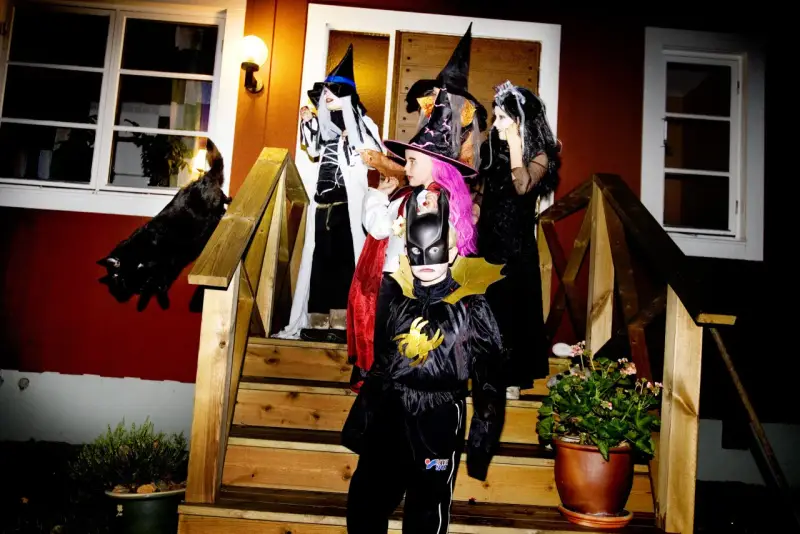 Barn utklädda till häxor och Batman förbereder sig för halloween helg. En svart katt smyger på trappan.