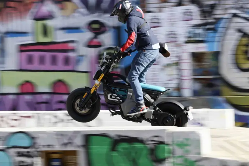 Młody mężczyzna na elektrycznym motocyklu BMW CE02 wykonuje skok na tle kolorowego graffiti.