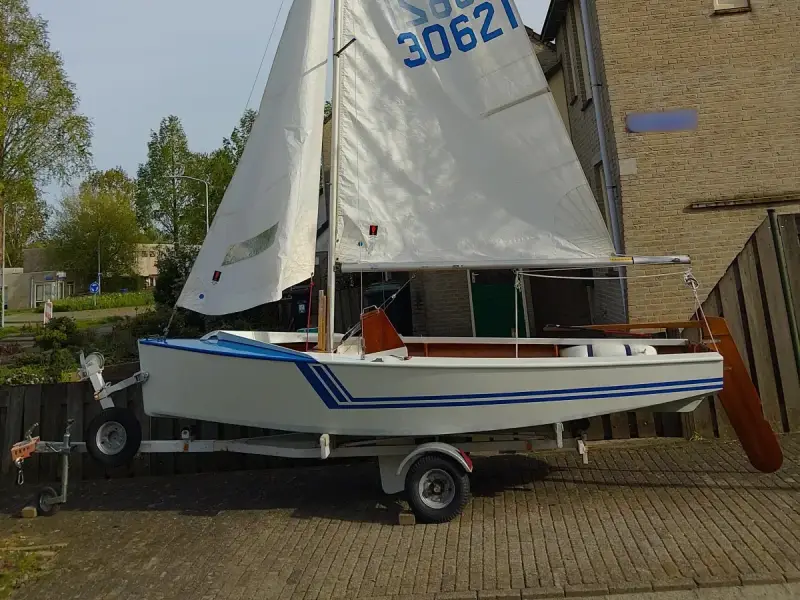 Un petit voilier blanc et bleu, un vaurien bateau prêt pour l'aventure, est sur sa remorque.