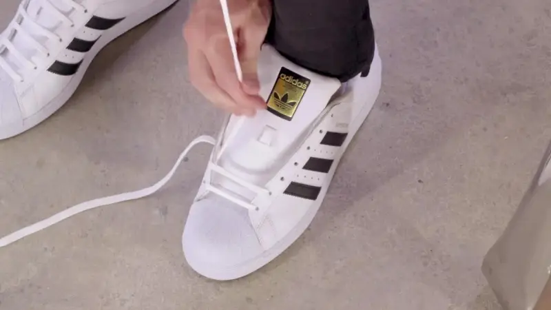 Pokazuję, jak wiązać sznurówki w adidasach Superstar. Białe sznurówki przeplatane przez czarne paski.