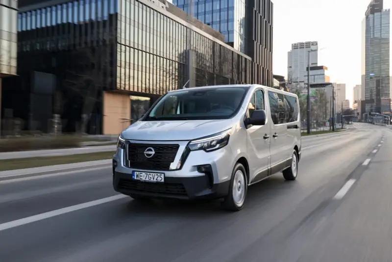 Srebrny van Nissan, jeden z najnowszych nissan modele, jedzie ulicą w nowoczesnym mieście.