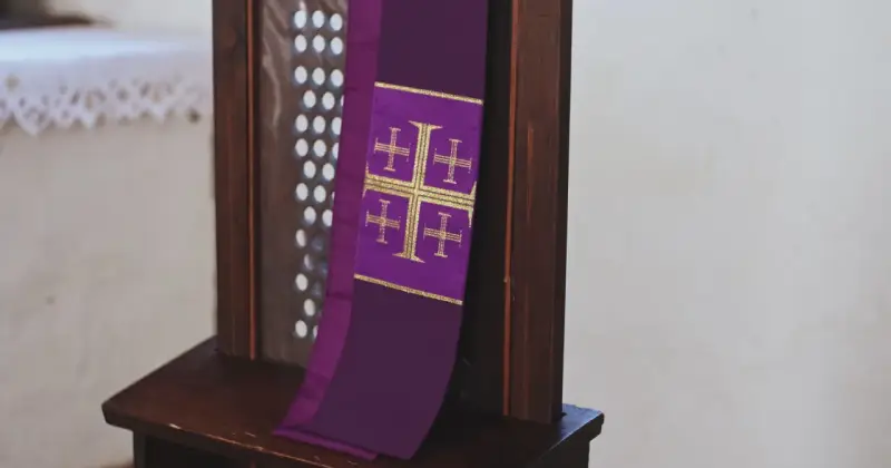 Fioletowa stuła z krzyżami, symbol przygotowania do spowiedzi wielkanocnej, wisi na drewnianej kratce konfesjonału.