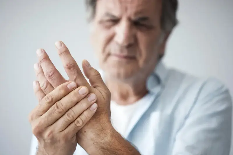 Mann hält seine Hand, da seine Finger schmerzen beim Beugen.