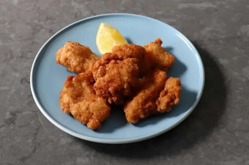 Chrupiący kurczak karaage na niebieskim talerzu, z kawałkiem cytryny.