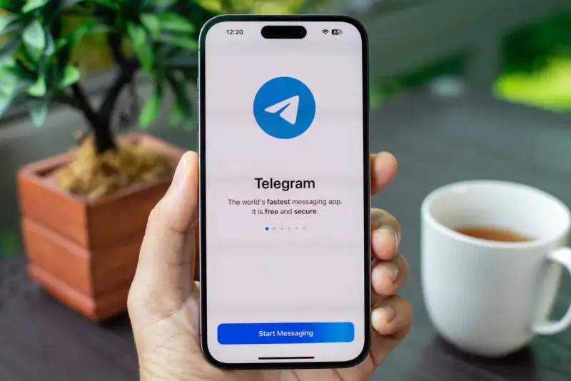Dłoń trzyma smartfon z otwartą aplikacją Telegram. Na ekranie widnieje logo i napis "Telegram. The world's fastest messaging app. It is free and secure.