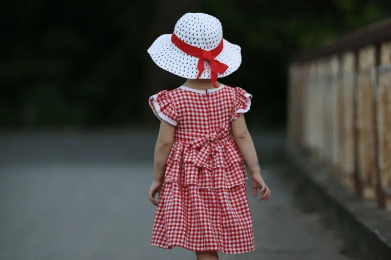 Dziewczynka w sukience w kratkę i kapeluszu z czerwoną wstążką, styl inspirowany modą lat 60.