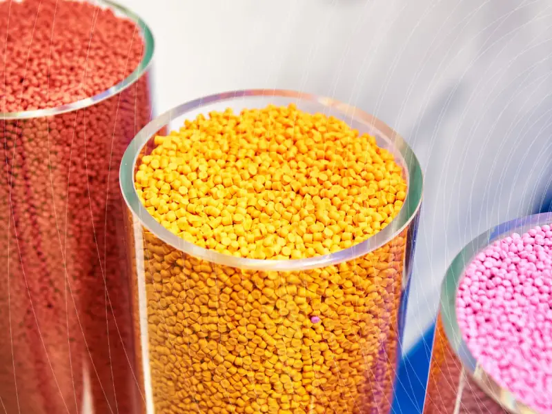 Trzy przezroczyste cylindry wypełnione kolorowymi granulkami plastiku: czerwonym, żółtym i różowym.