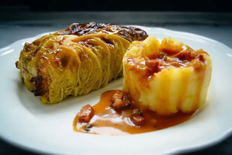 Ein goldbraunes Kohlrouladen-Rezept auf einem Teller, serviert mit Kartoffelpüree und einer herzhaften Sauce.