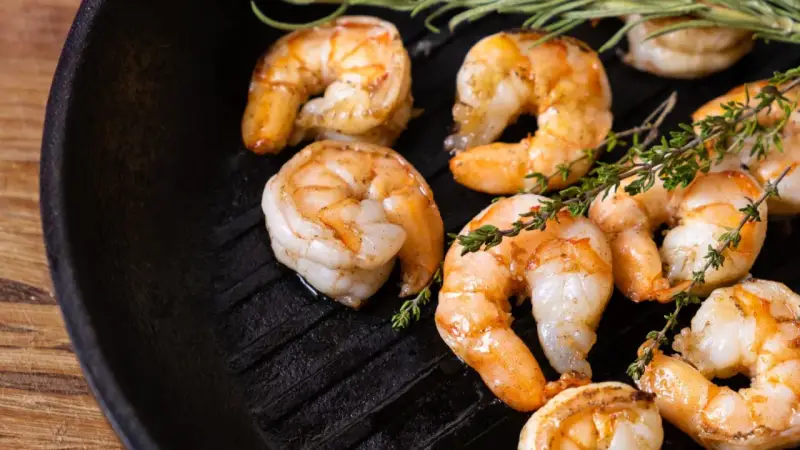 Gambas a la plancha jugosas y doradas, con ramitas de tomillo fresco sobre una sartén de hierro fundido.
