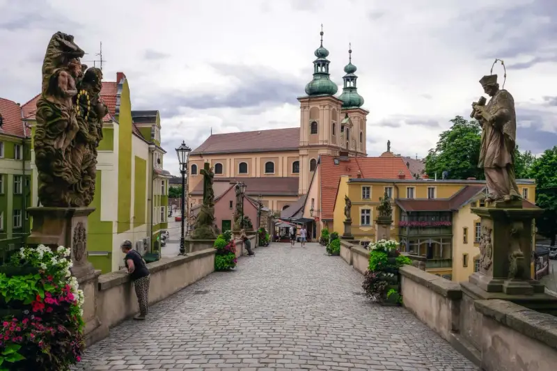 Kamienny most z rzeźbami i barokową architekturą, w tym kościołem z zielonymi kopułami. To piękne ziemia kłodzka atrakcje.