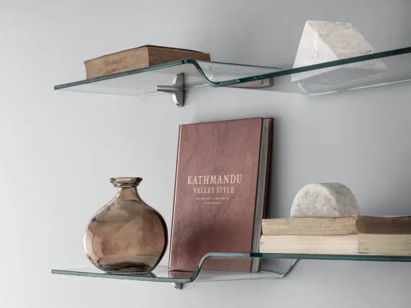 Idee mensole ingresso: vetro curvo con libri antichi, vaso ambrato e scultura in marmo.
