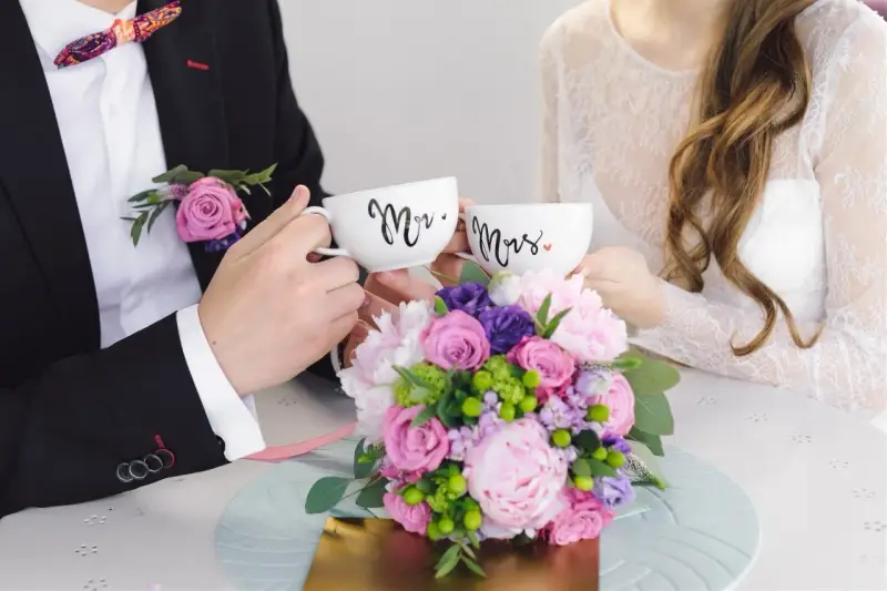 Para świętuje 4 rocznicę ślubu, trzymając kubki "Mr." i "Mrs." na tle bukietu kwiatów.