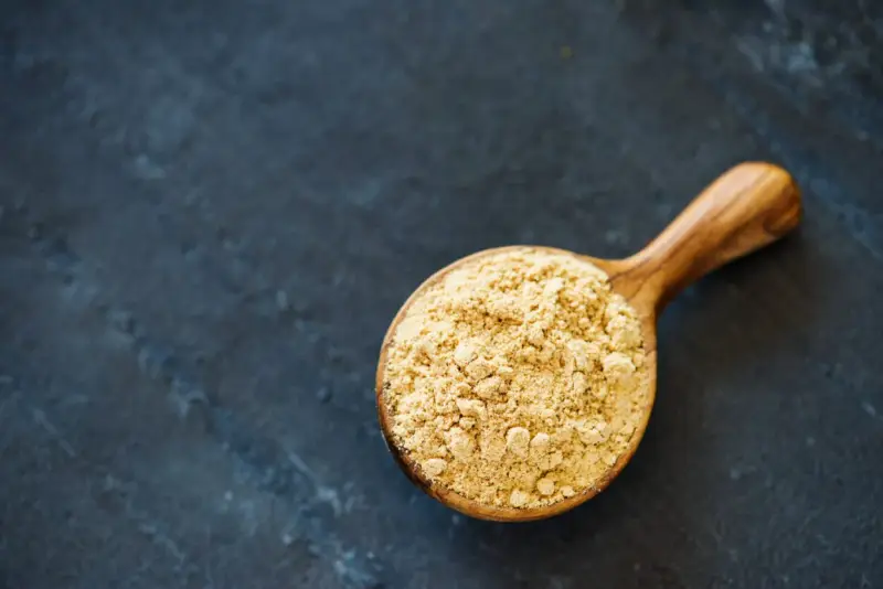 Cuillère en bois remplie de poudre de maca, évoquant ses nombreux bienfaits pour la santé et l'énergie.
