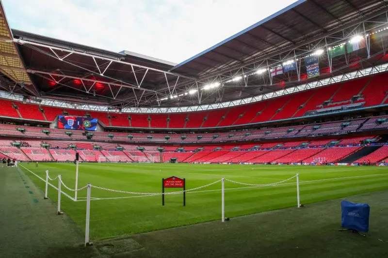 Pusta, czerwona trybuna stadionu Wembley, największego stadionu na świecie, z zieloną murawą i tabliczką "Prosimy nie wchodzić na trawę".