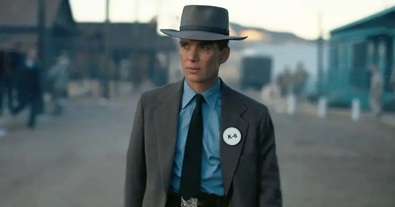 Julius Robert Oppenheimer w kapeluszu i garniturze, z odznaką K-6, w scenerii przypominającej miasteczko.