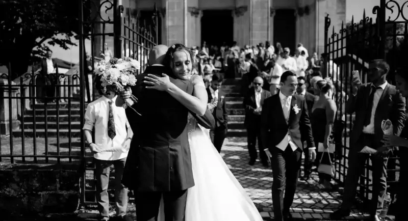 Un couple s'embrasse devant une église, entouré d'invités. Un jeune garçon tient un bouquet. Ce moment est le fruit d'un savant **rétroplanning mariage**.
