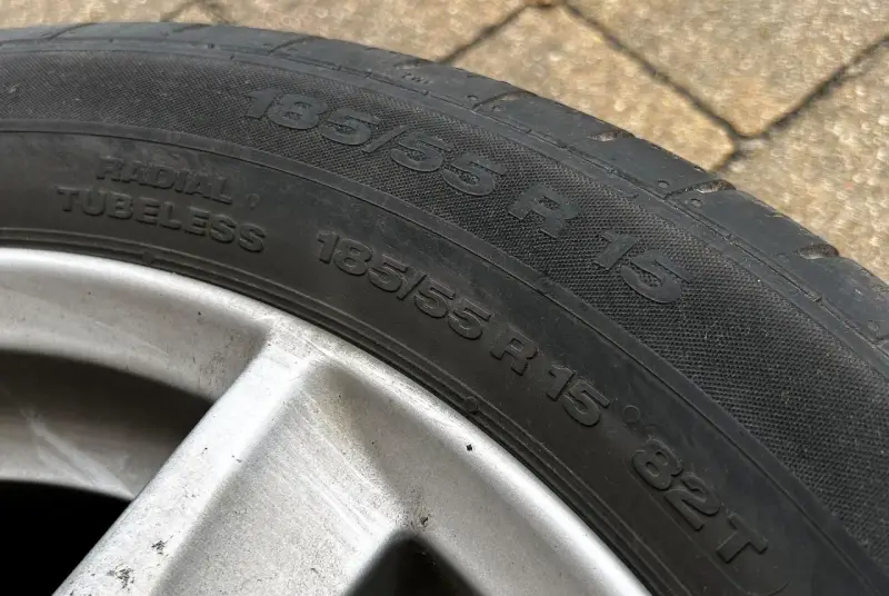 Oznaczenie opon: 185/55 R15, Radial Tubeless. Widoczna felga aluminiowa.