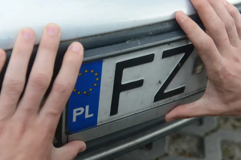 Dłonie trzymają tablicę rejestracyjną z oznaczeniem PL i literami FZ. Może to być związane z czasowe wyrejestrowanie pojazdu.