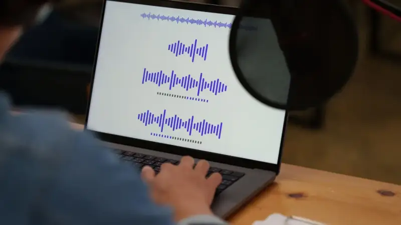 Osoba pracuje przy laptopie, na ekranie widoczne są wykresy fal dźwiękowych, co może być związane z tworzeniem adlibów.