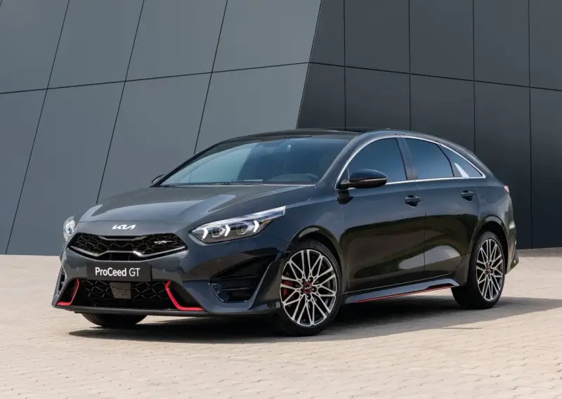 Stylowy, ciemnoszary Kia Proceed GT z czerwonymi akcentami i sportowymi felgami, zaparkowany przed nowoczesnym budynkiem.