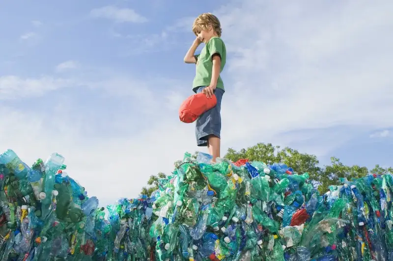 Chłopiec stoi na górze sterty plastikowych butelek, zastanawiając się, co to za pla.