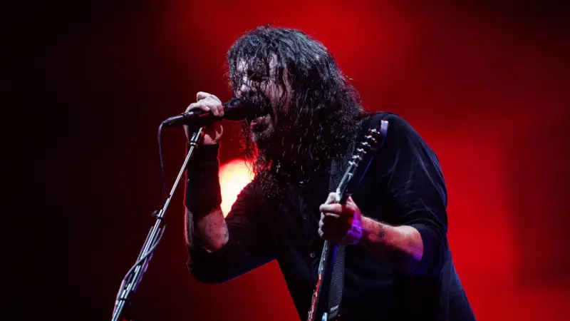 Dave Grohl z Foo Fighters na koncercie, śpiewający do mikrofonu i grający na gitarze.