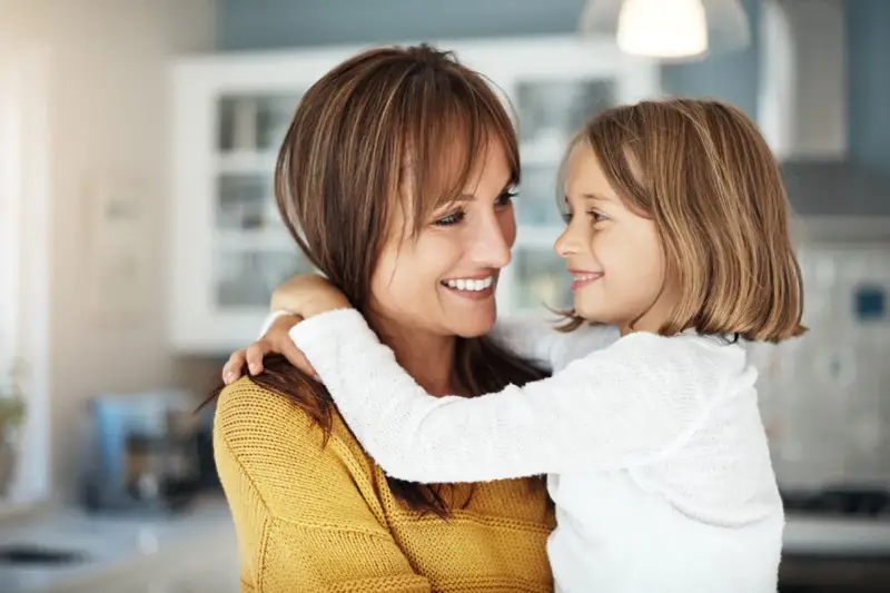 Uśmiechnięta mama i córka przytulają się, emanując ciepłem i bliskością. To kwintesencja rodzicielstwa bliskości.