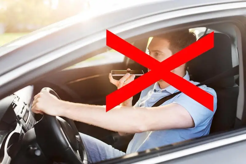 Uomo al volante che usa il cellulare, vietato dall'art. 173 CDS. La croce rossa indica il divieto.