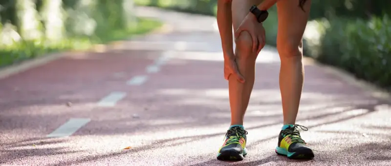 Läuferin hält schmerzendes Knie auf Laufbahn. Knieschmerzen nach Joggen sind ein häufiges Problem.