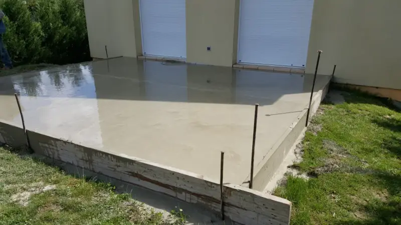 Dalle en béton fraîchement coulée pour une maison, avec coffrage en bois et ferraillage apparent. L'épaisseur de la dalle est visible.