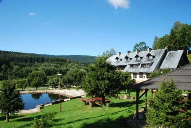 Budynek pensjonatu z kamiennym stawem i zielonym ogrodem w Górach Orlickich.