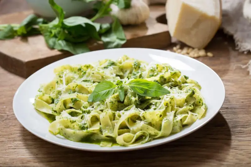 Talerz tagliatelle z aromatycznym pesto z rukoli, posypany parmezanem i udekorowany listkami bazylii.
