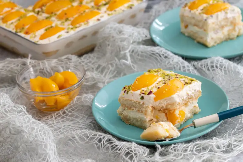 Delizioso tiramisù alle pesche, con strati di savoiardi, crema soffice e pesche sciroppate, guarnito con pistacchi.