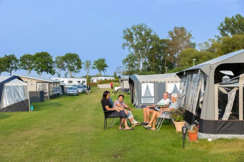 Familj njuter av en solig dag på en av Sveriges billiga campingar. Husvagnar och tält står uppradade på en grön gräsmatta.