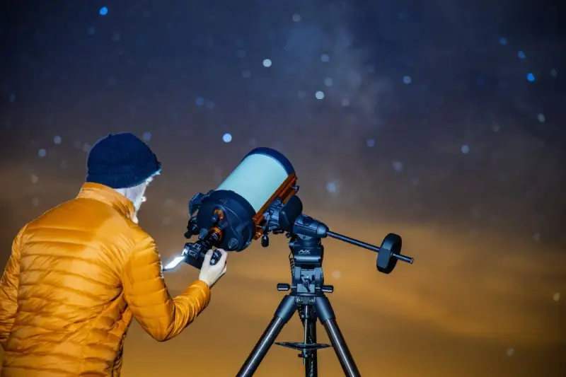 Mężczyzna w pomarańczowej kurtce ustawia aparat Canon EOS Ra do astrofotografii pod rozgwieżdżonym niebem.
