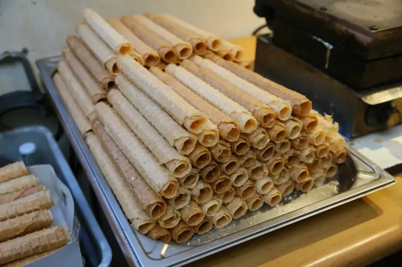 Stos kupnych wafli do rurek z kremem, obok gorącej gofrownicy.