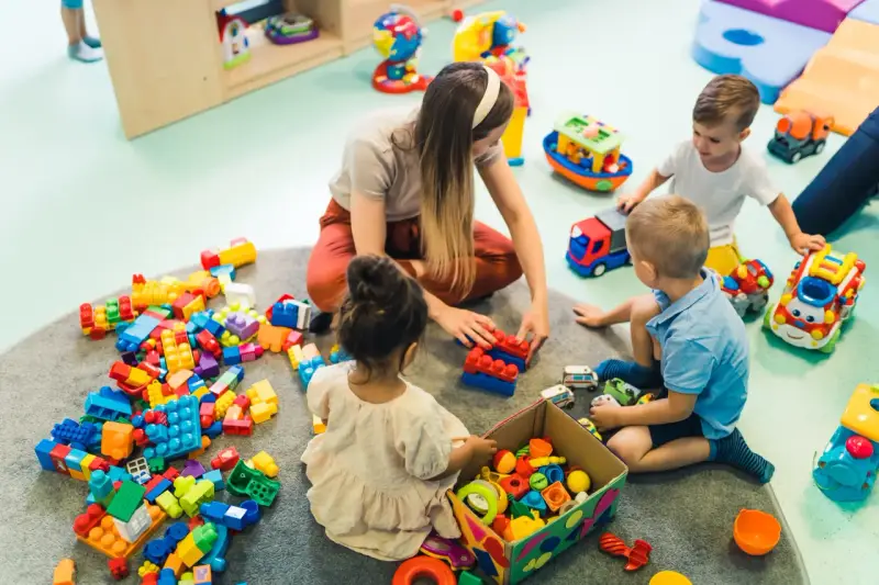Dzieci bawią się klockami z opiekunką. Czy za żłobek się płaci? To pytanie zadają sobie rodzice, widząc radosne chwile swoich pociech.