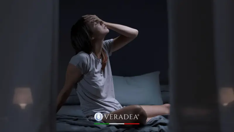 Donna sveglia di soprassalto nel letto, con la mano sulla fronte, soffre di sudorazione notturna. Cerca rimedi per dormire serenamente.