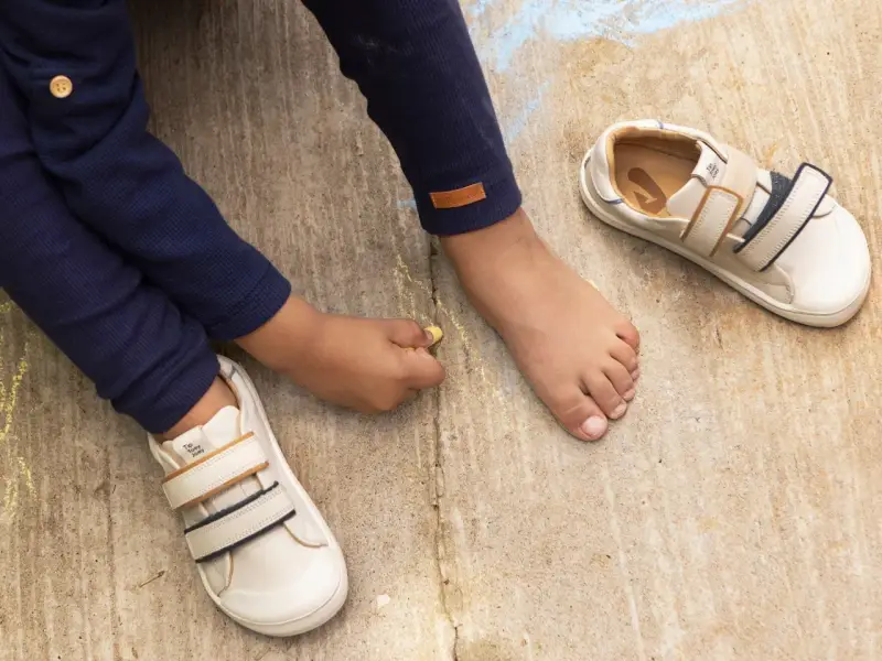 Niño descalzo dibuja con tiza junto a sus zapatos de calzado fisiológico, listos para la aventura.