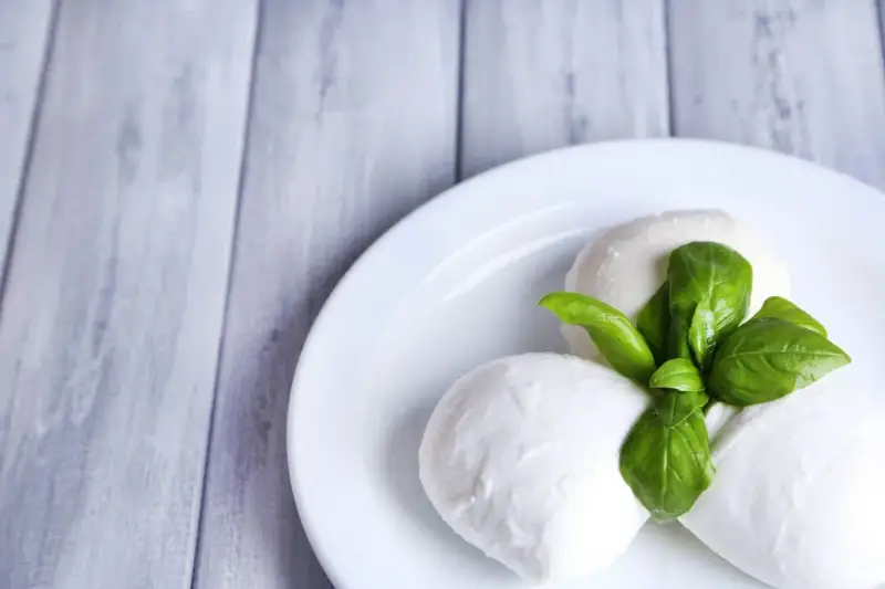 Trzy kulki serka mozzarella z listkami bazylii na białym talerzu. Idealne do sałatki, znasz ser mozzarella kcal?