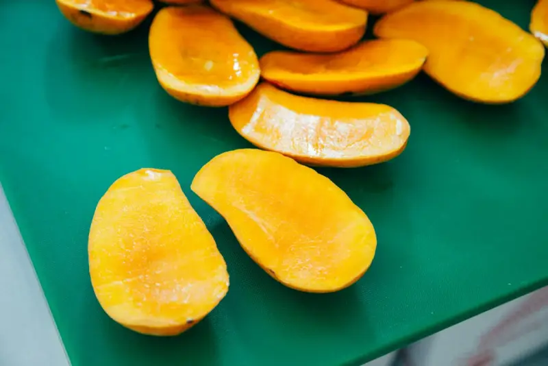 Pokrojone w łódeczki, soczyste mango w intensywnym kolorze, jakby w ciąży z owocową obfitością, leżą na zielonej desce.