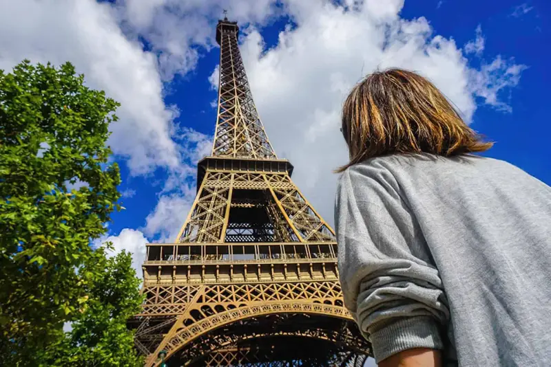 Persona admira la imponente Torre Eiffel bajo un cielo azul con nubes.