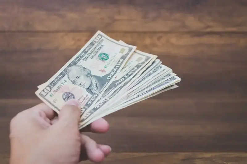 Dłoń trzyma plik banknotów dziesięciodolarowych. To może być zapłata za trzynastkę lub po prostu nagroda.