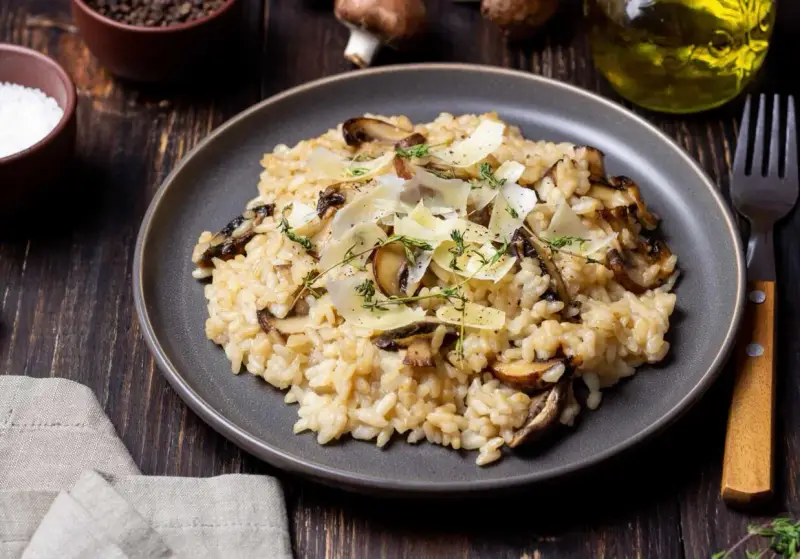 Kremowe risotto z pieczarkami, posypane parmezanem i ziołami, na ciemnym talerzu.