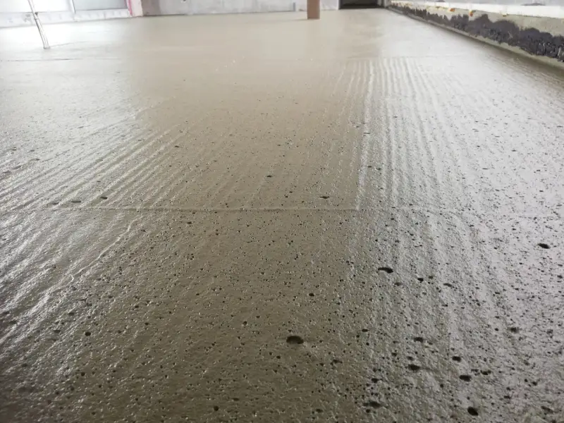 Świeżo wylany, wilgotny **pianobeton** na budowie, z widocznymi śladami po zacieraniu i drobnymi pęcherzykami powietrza.